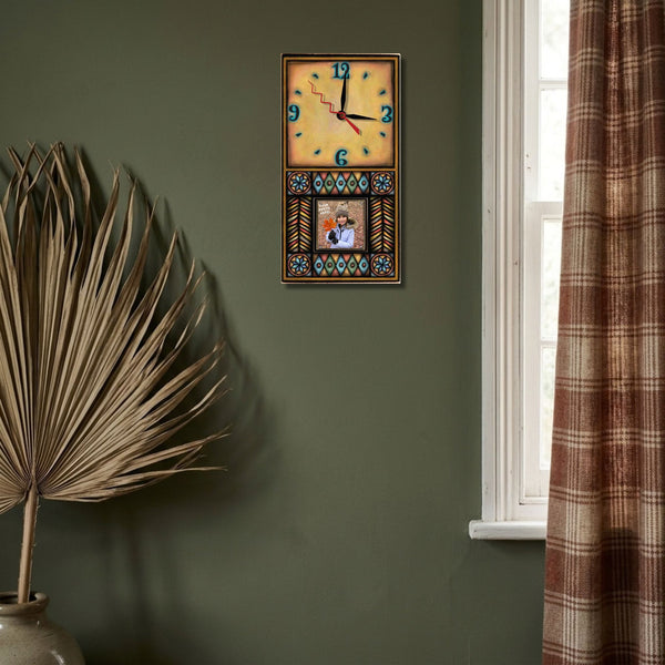 Brown Motif geometric picture frame wood wall clock hanging on a deep olive green wall beside a dried palm leaf and a rust plaid curtain