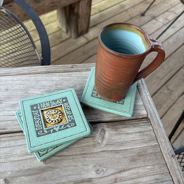 Handmade turquoise ceramic Everyday a New Story Begins coaster with crazed glass center styled with a mug on a matching ceramic coaster by Macone Clay.