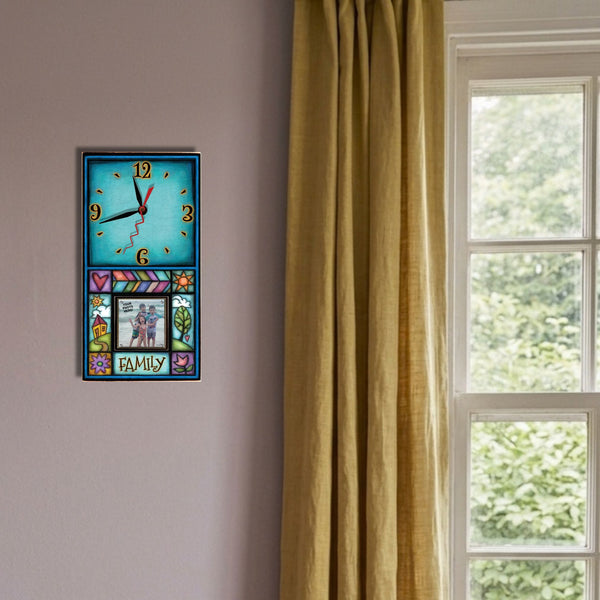 Family picture frame wood wall clock hanging on a dusty lavender wall beside a wooden blanket ladder and a terracotta linen curtain