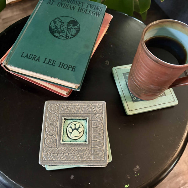 Handmade gray ceramic paw print coaster with crazed glass center styled with a mug on a matching ceramic coaster by Macone Clay.