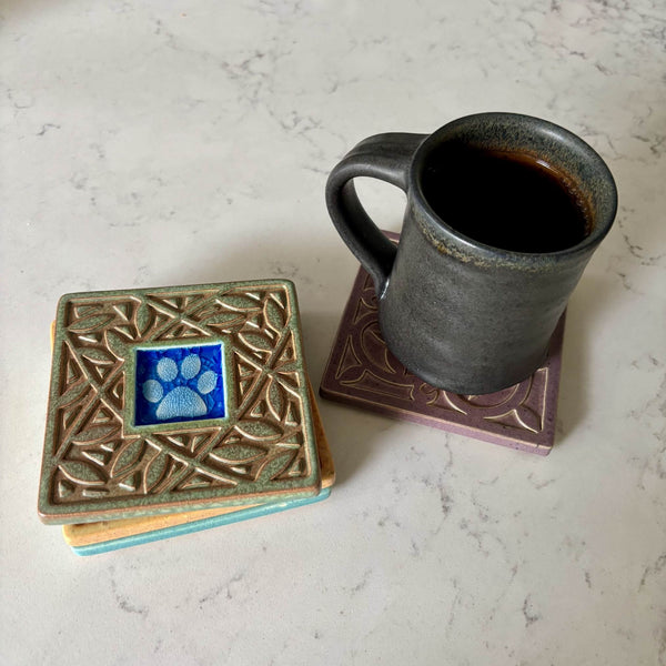 Handmade ceramic paw print coaster with crazed glass center and leaf border styled with a mug on a matching ceramic coaster by Macone Clay