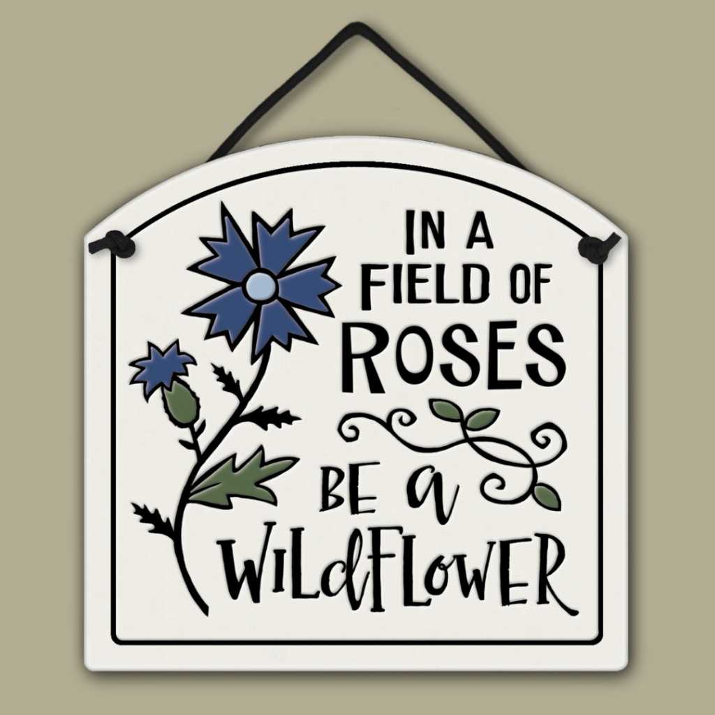 Ceramic wall tile with blue wildflower illustration and the quote ‘In a field of roses be a wildflower.’