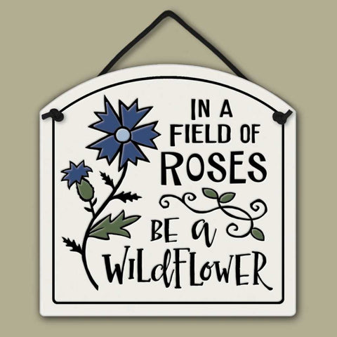Ceramic wall tile with blue wildflower illustration and the quote ‘In a field of roses be a wildflower.’