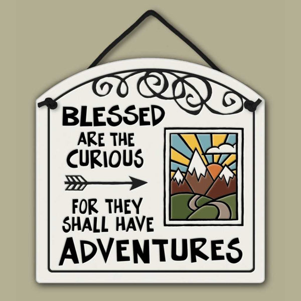 Decorative ceramic wall tile with the quote ‘Blessed are the curious for they shall have adventures’ and a colorful mountain sunrise illustration.