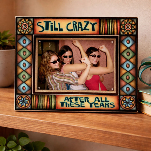 Funny friendship picture frame with quote Still crazy after all these years displayed on a wooden shelf featuring colorful Michael Macone artwork and 4 x 6 photo.