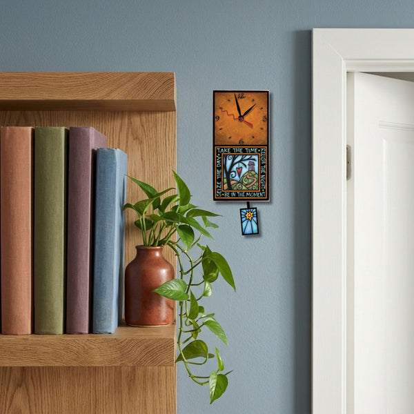 Take the Time handmade pendulum wall clock hanging on a bright blue wall beside a white bookshelf in a colorful home office