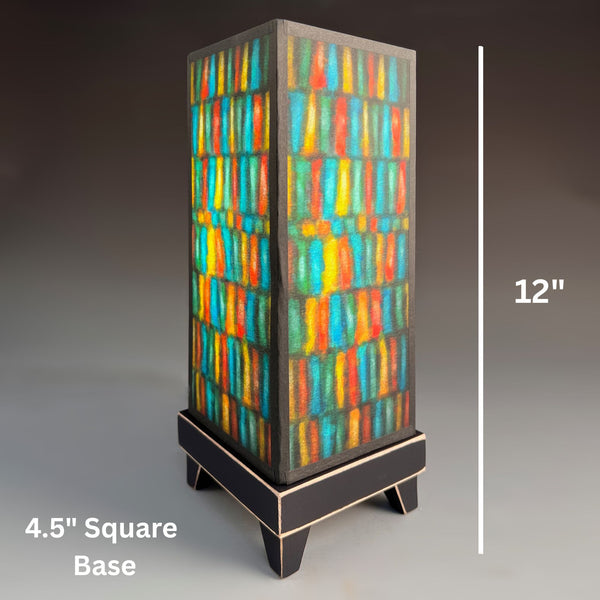 Vertical Stripes mood lamp, a tall rectangular table lamp with a dark wood base and colorful striped stained-glass style paper shade in teal, yellow, orange, and green showing dimensions 4.5" x 12"