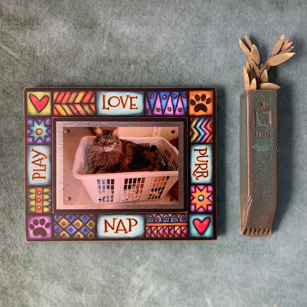 Cat picture frame with quote Love Purr Nap Play hanging on a wall with colorful Michael Macone artwork and magnetic 4 x 6 cat photo display.
