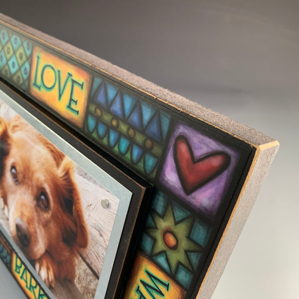 Corner detail of dog picture frame artwork showing colorful Michael Macone illustration and paw print design around quote Love Wag Bark Play.