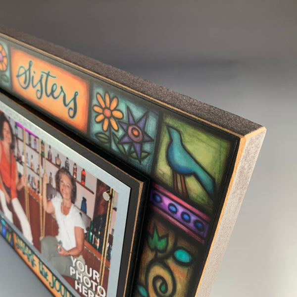 Corner detail of Sisters Share the Journey quote picture frame by Michael Macone showing colorful folk art design and handcrafted Macone Clay frame